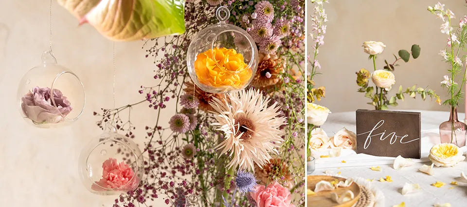 Blomsterarrangemang med rosa, lavendel och orange rosor inuti glaskulor. Torkade blommor och grönska omger orbs. I närheten visar ett dukat bord en femskylt med färska blommor och kronblad utspridda.